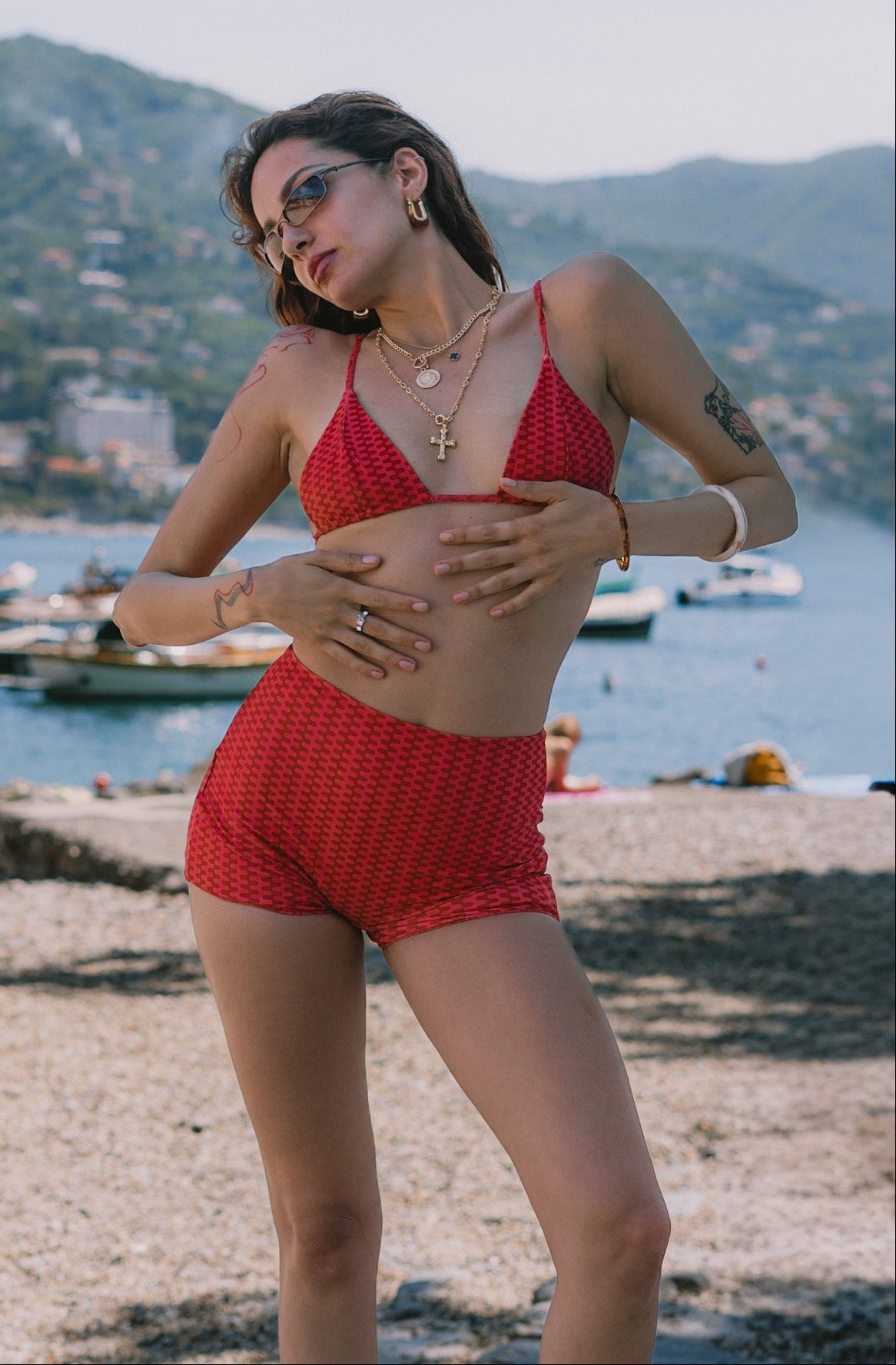Woman in a red bikini standing on a beach with mountains and water in the background